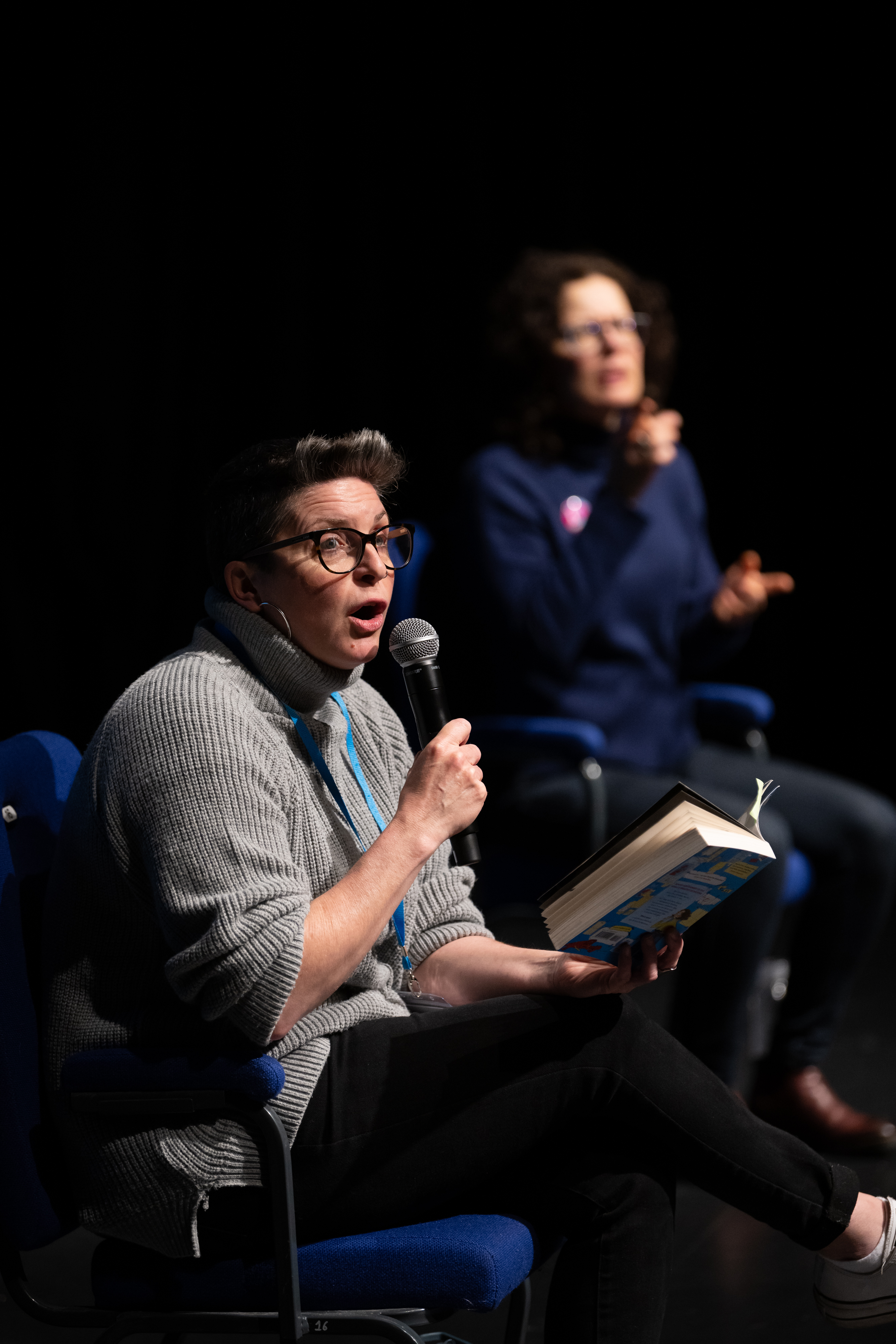 A woman holds a book and speaks into a microphone