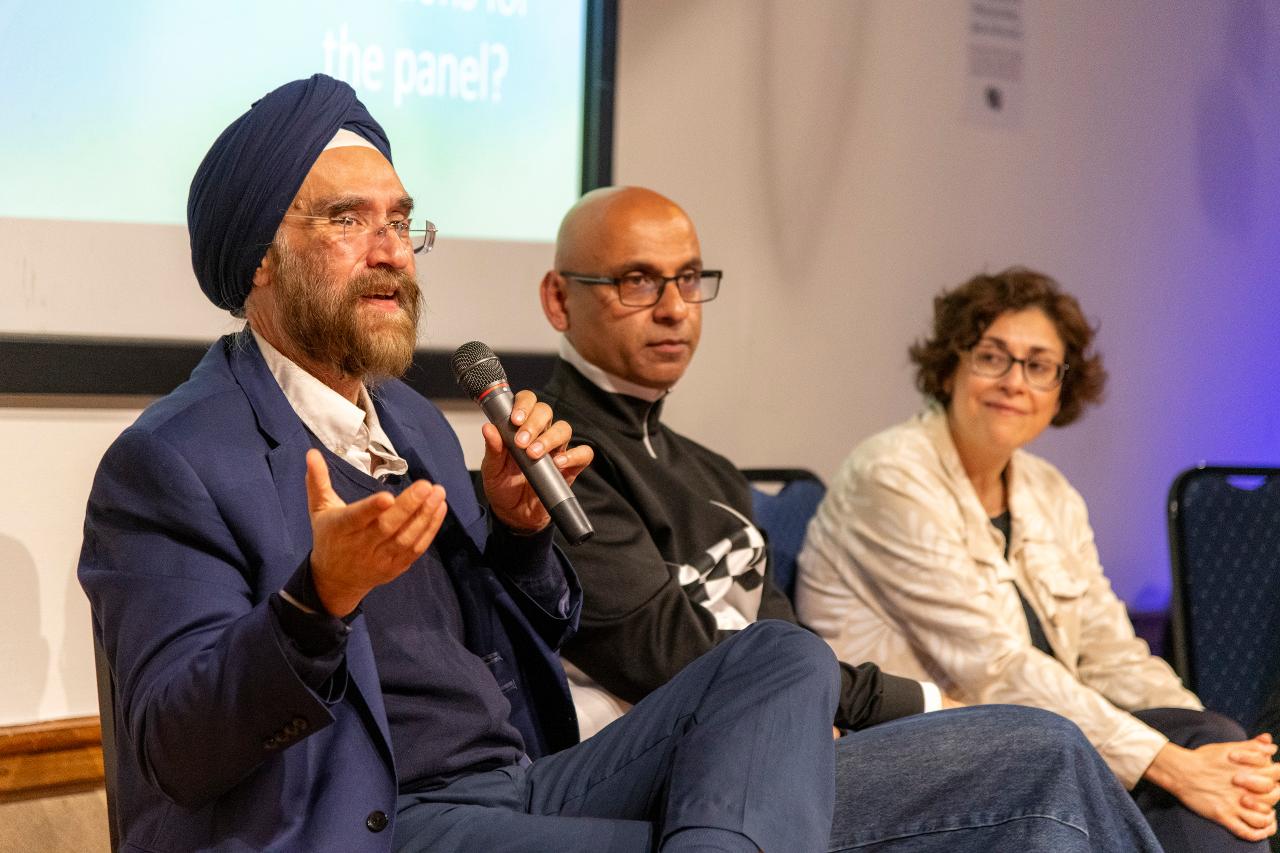 Three speakers sat on a panel at a Resonate Late event. One holds a microphone, the others are listening. 