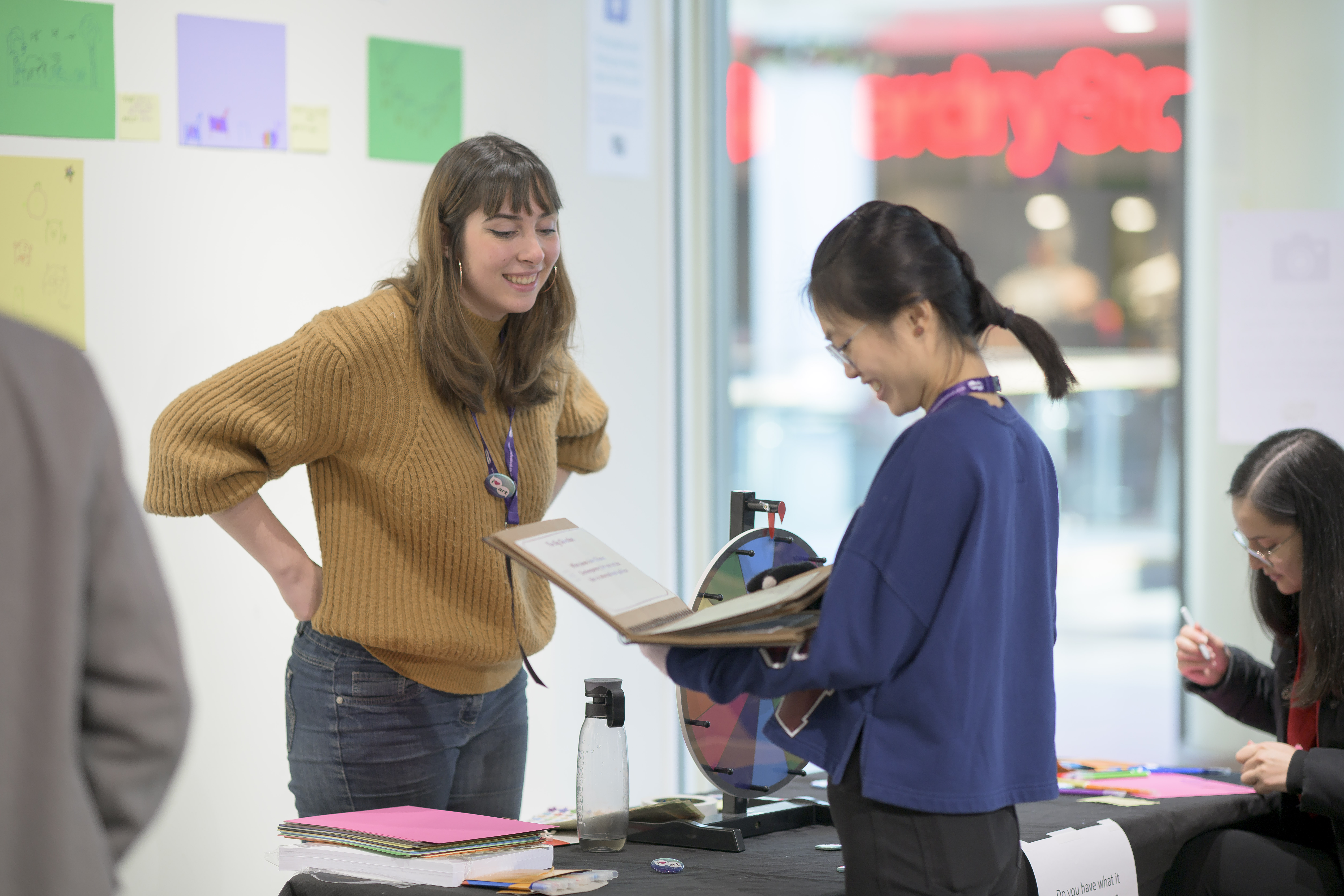 An undergraduate student stands behind a table and talks about their research to an attendee. 