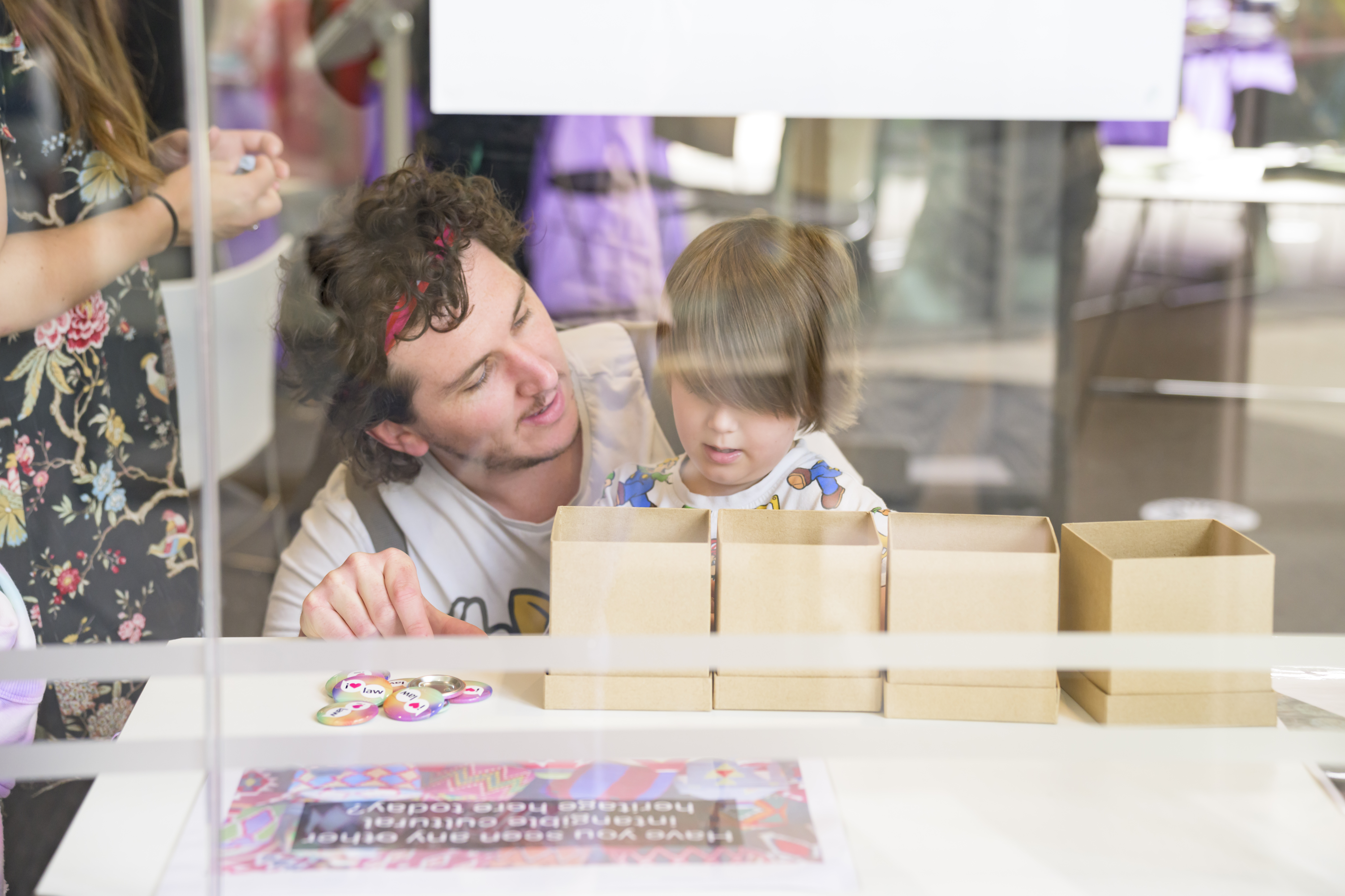 A child and their adult stood by a table looking into small boxes