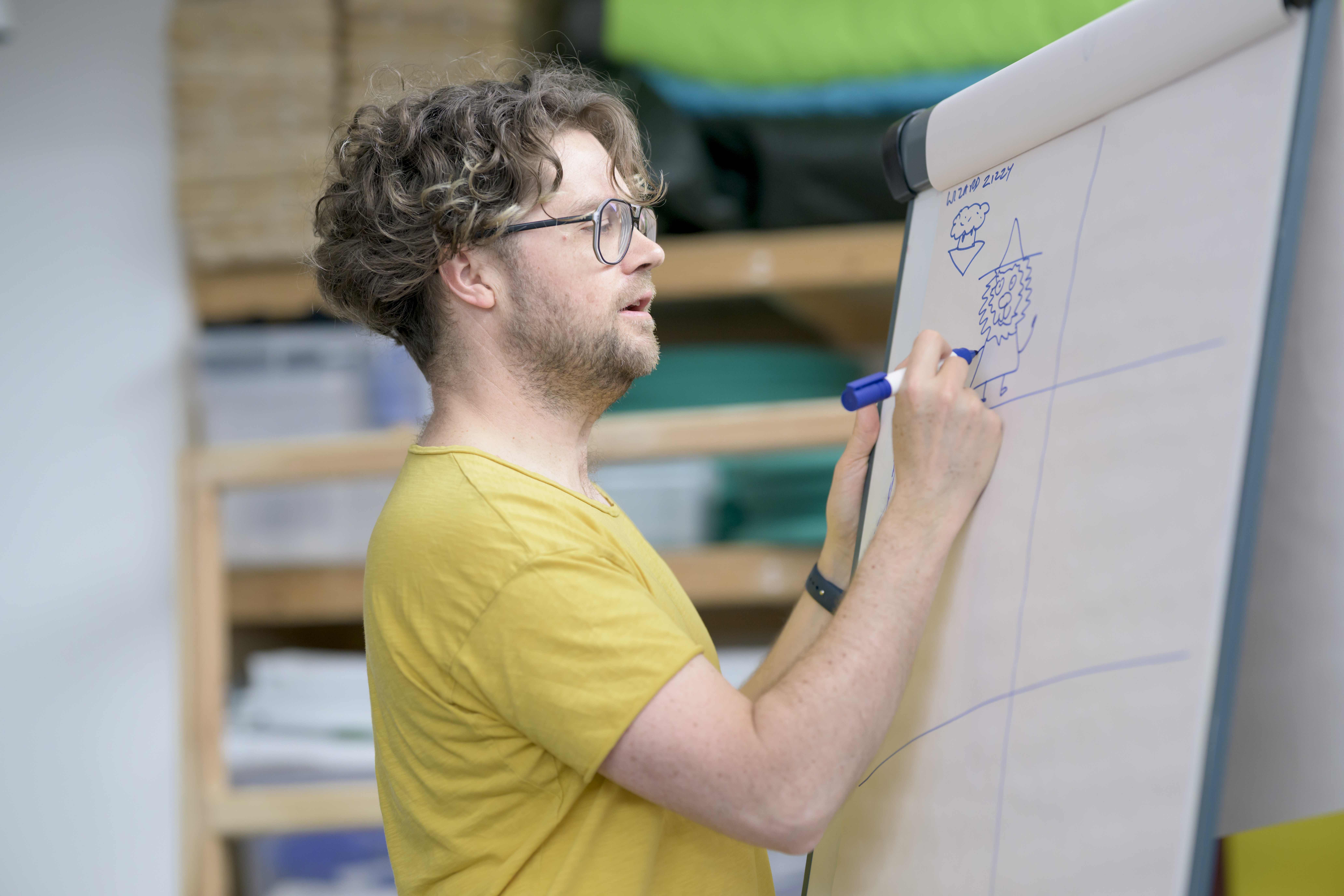 A man in a yellow t-shirt is writing on flip chart paper.