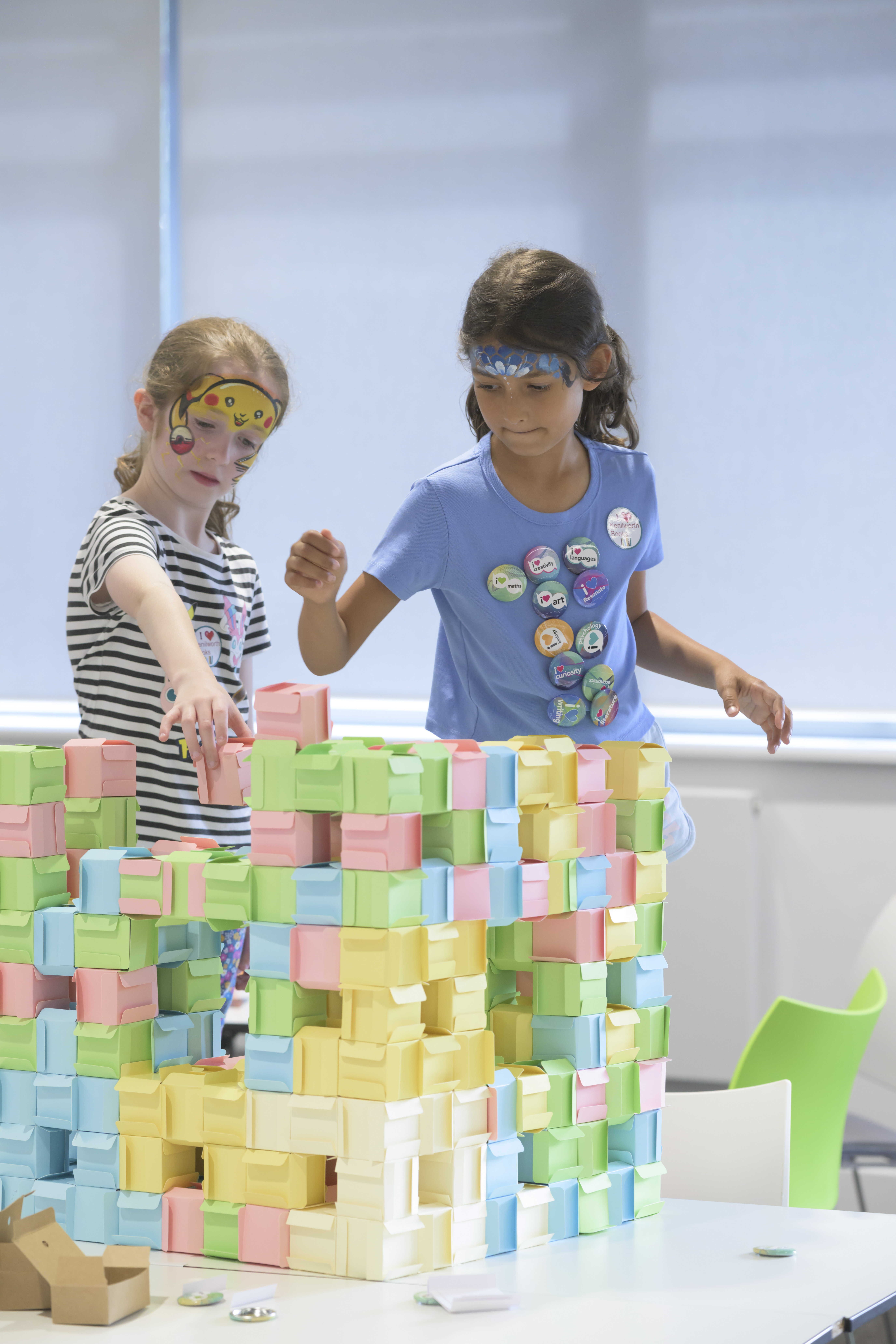 Two children stacking paper folded cubes into a larger cube structure with gaps in it. 