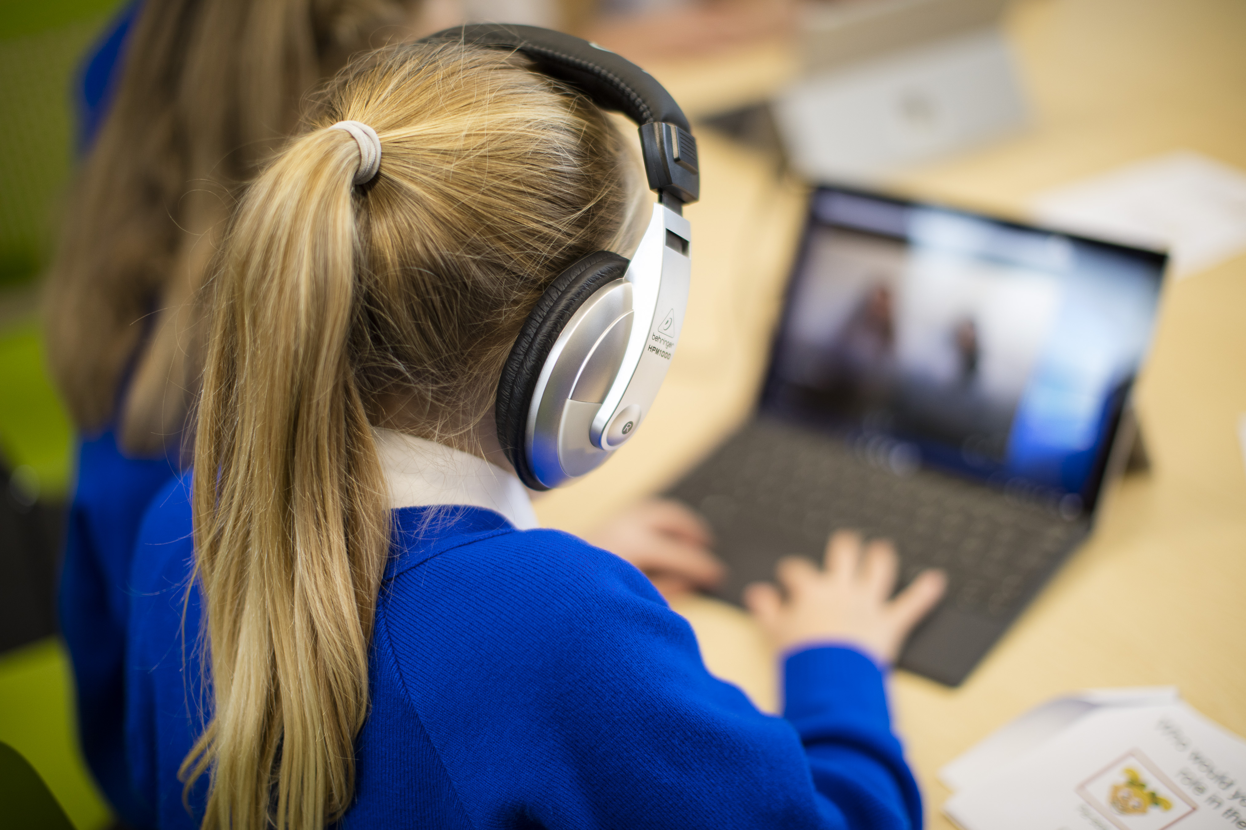 Child with headphones typing on a laptop.