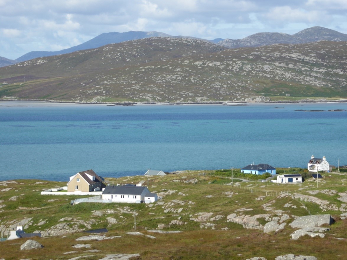 Houses on a green rocky hillside with the sea and hills in the background