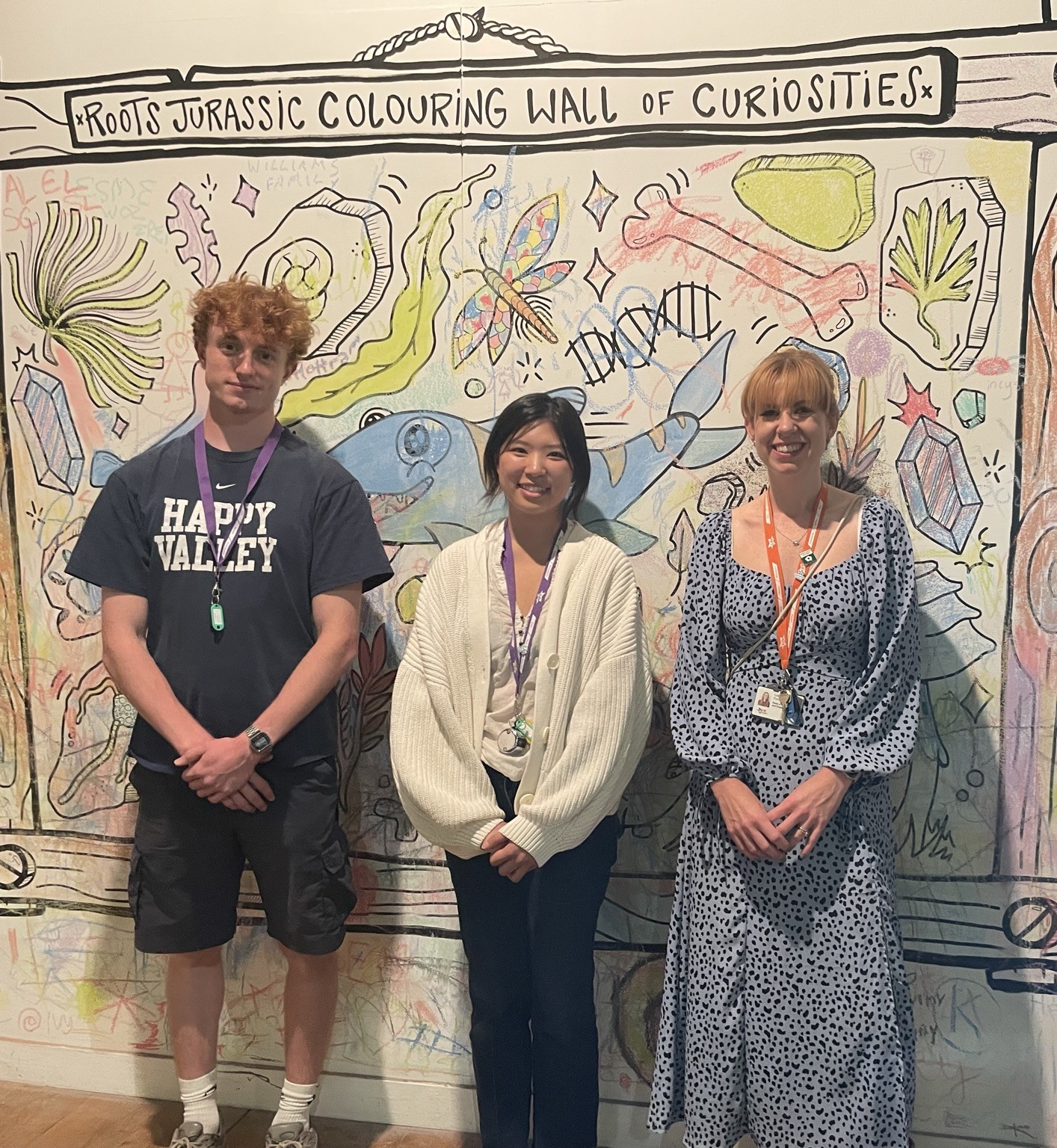 Joss Wozencroft and Ju-Eun Kang standing against a 'Jurassic colouring wall' with lots of bright colouring