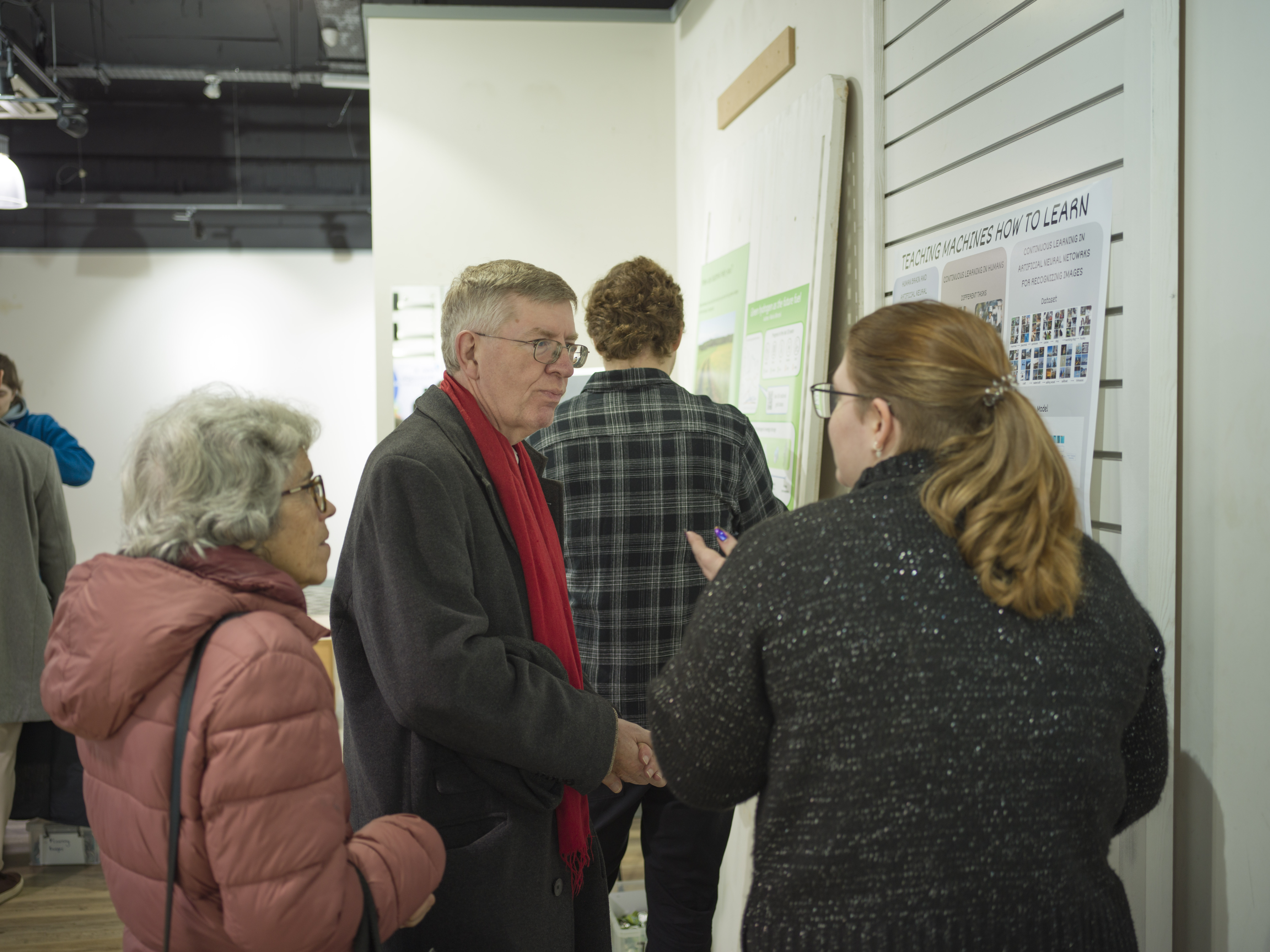 A student talks to two members of the public next to their poster.