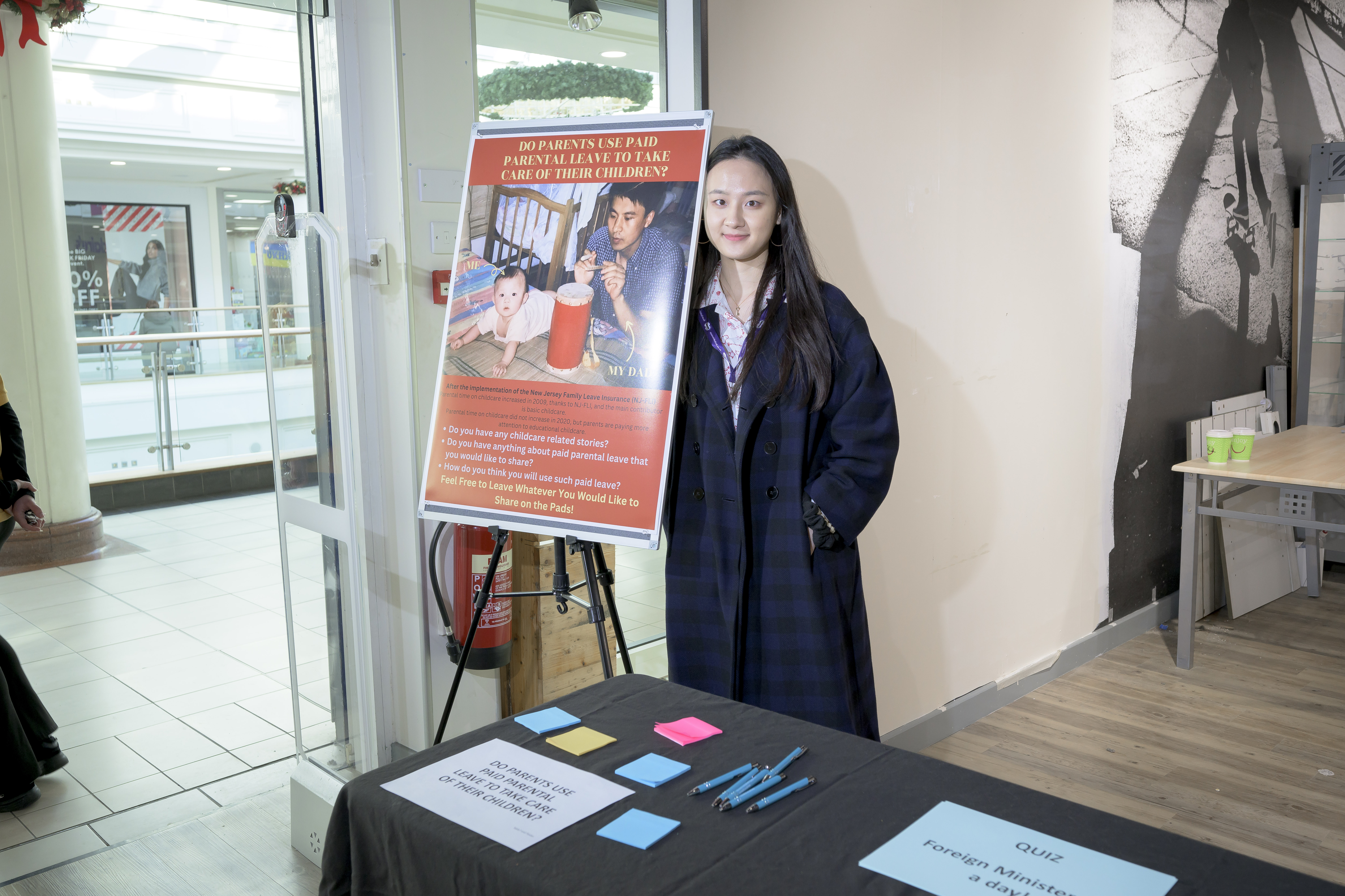 A student standing next to a poster which has a photo of a father and young child on it. 