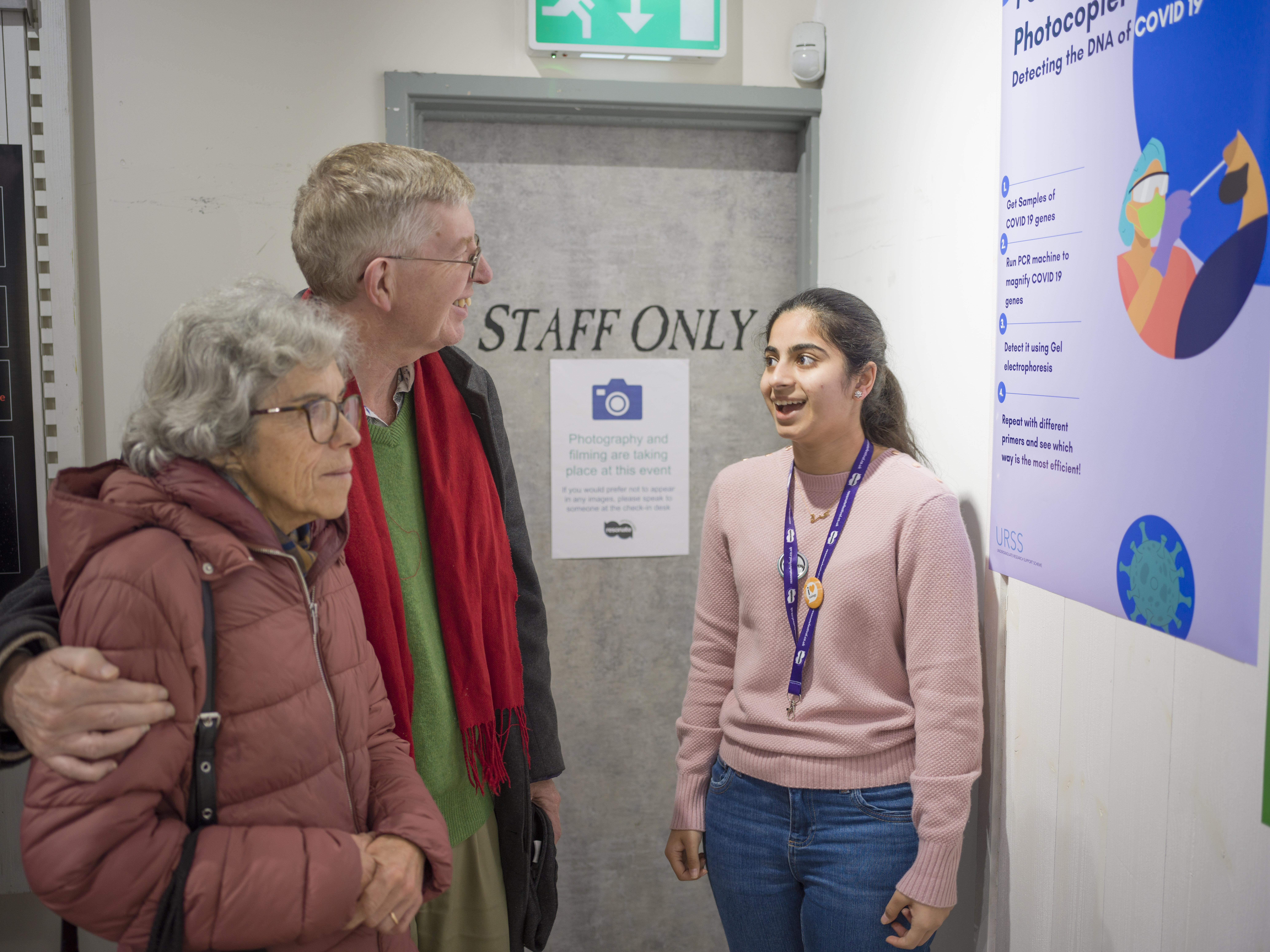 A student talks to two visitors about their poster. 