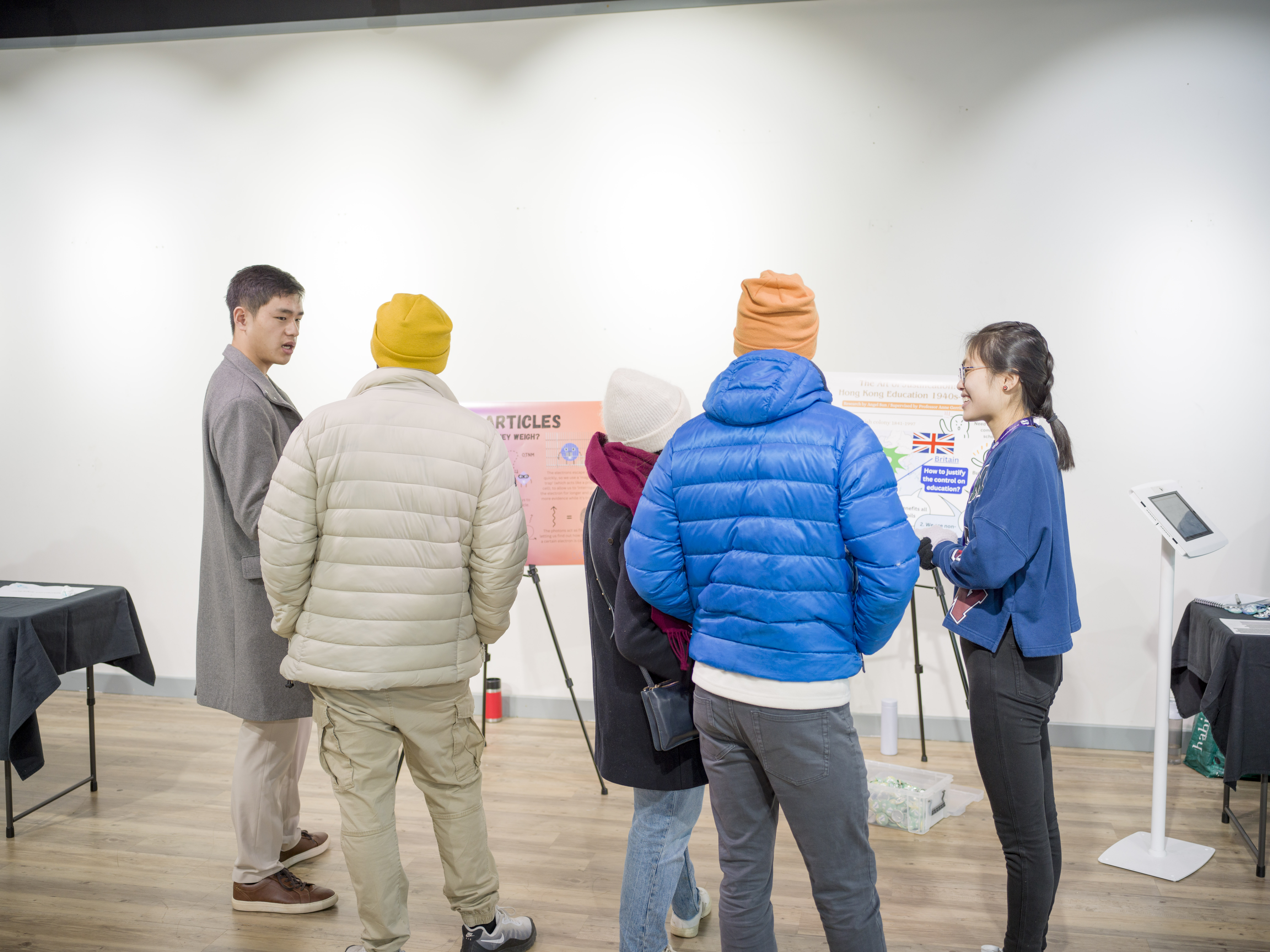 Two students next to two posters, talking to three people in coats and hats. 