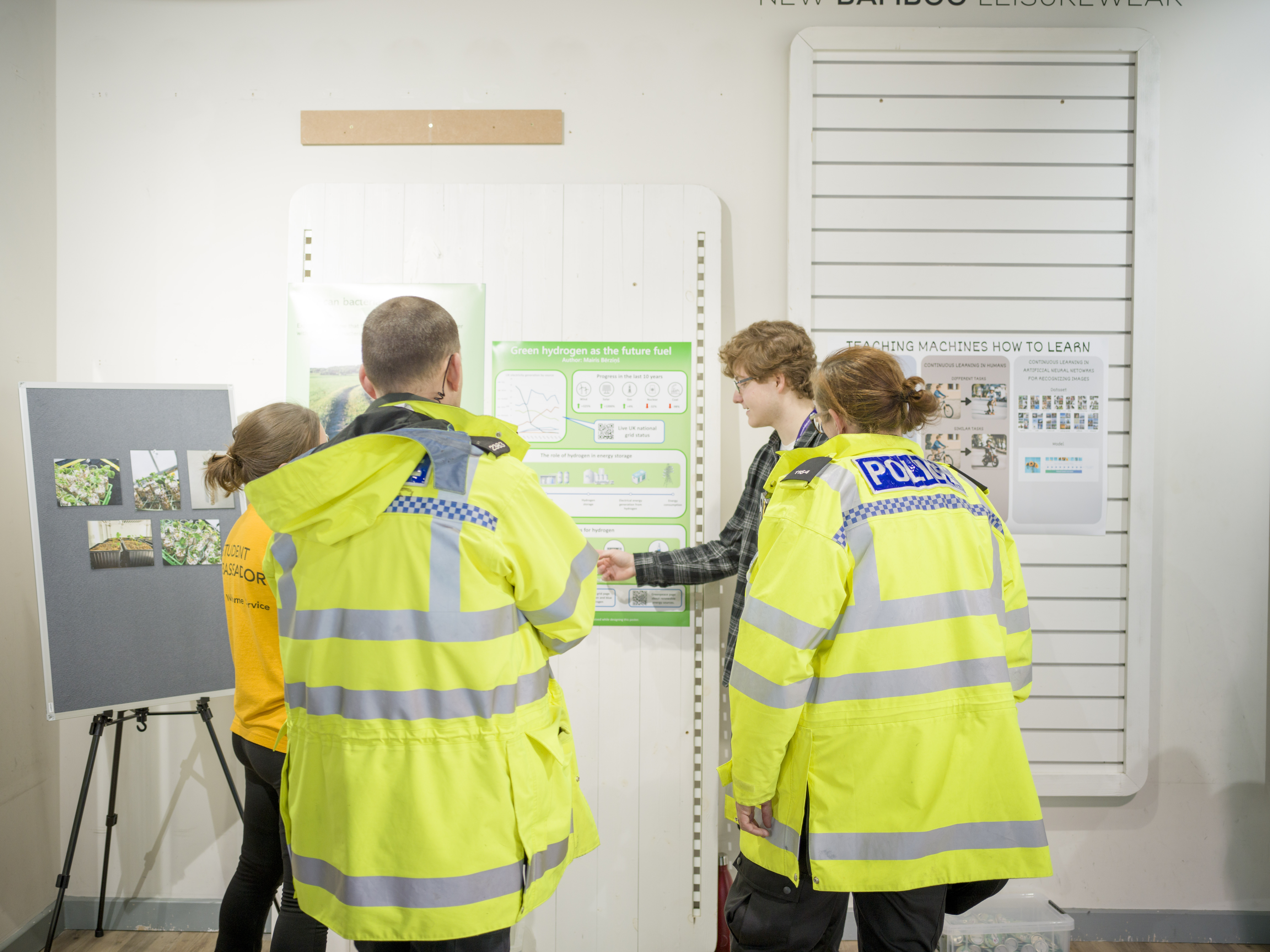 A student talks about their green poster with another student and two police officers in fluorescent jackets.