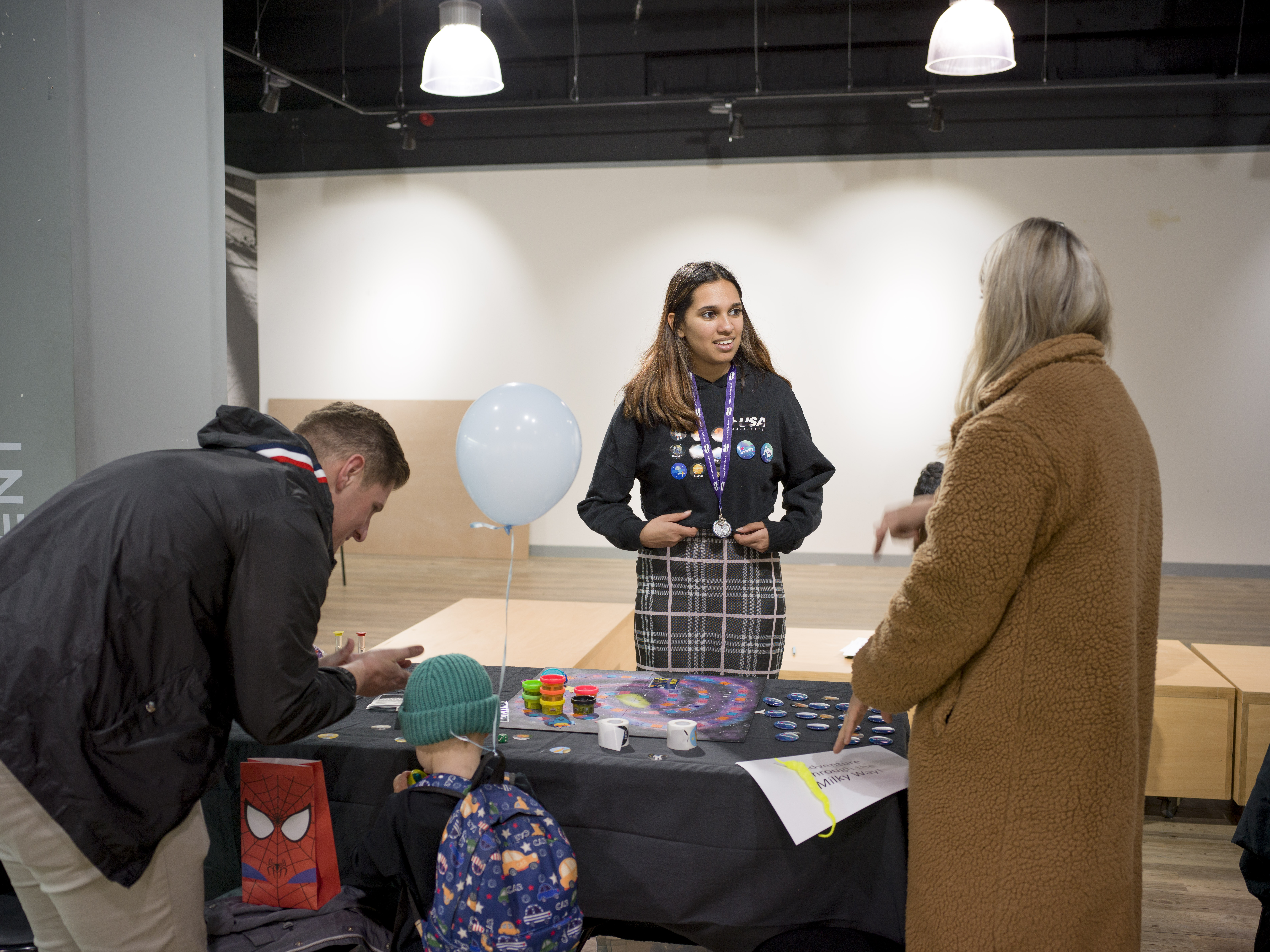 A young child is playing a board game with an adult. Another adult talks to a Warwick student about the board game. 