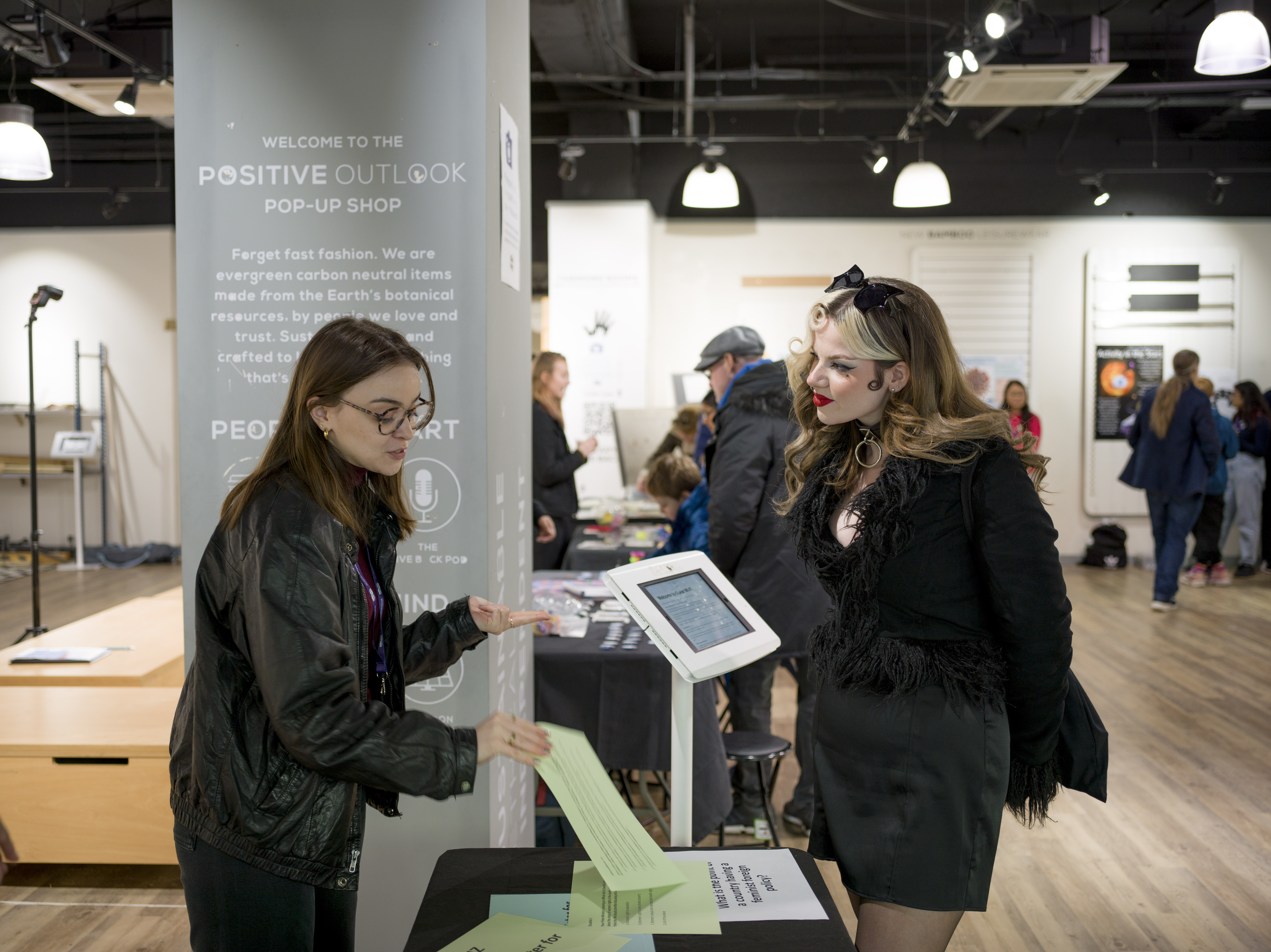 A student talks to a visitor about their quiz, which is on coloured paper and on an iPad. 