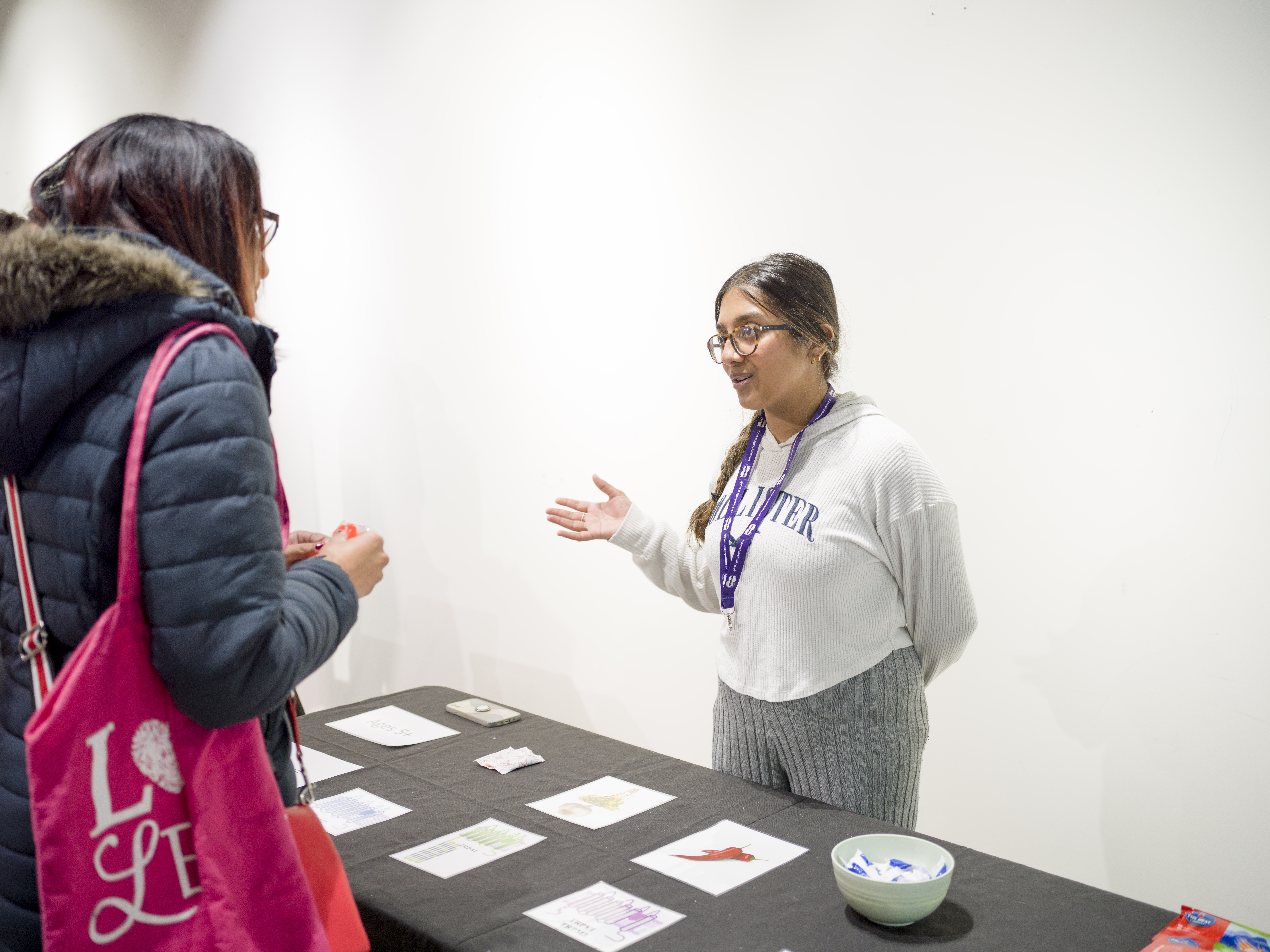 A student talking to an adult. There are different objects and foods on the table. 