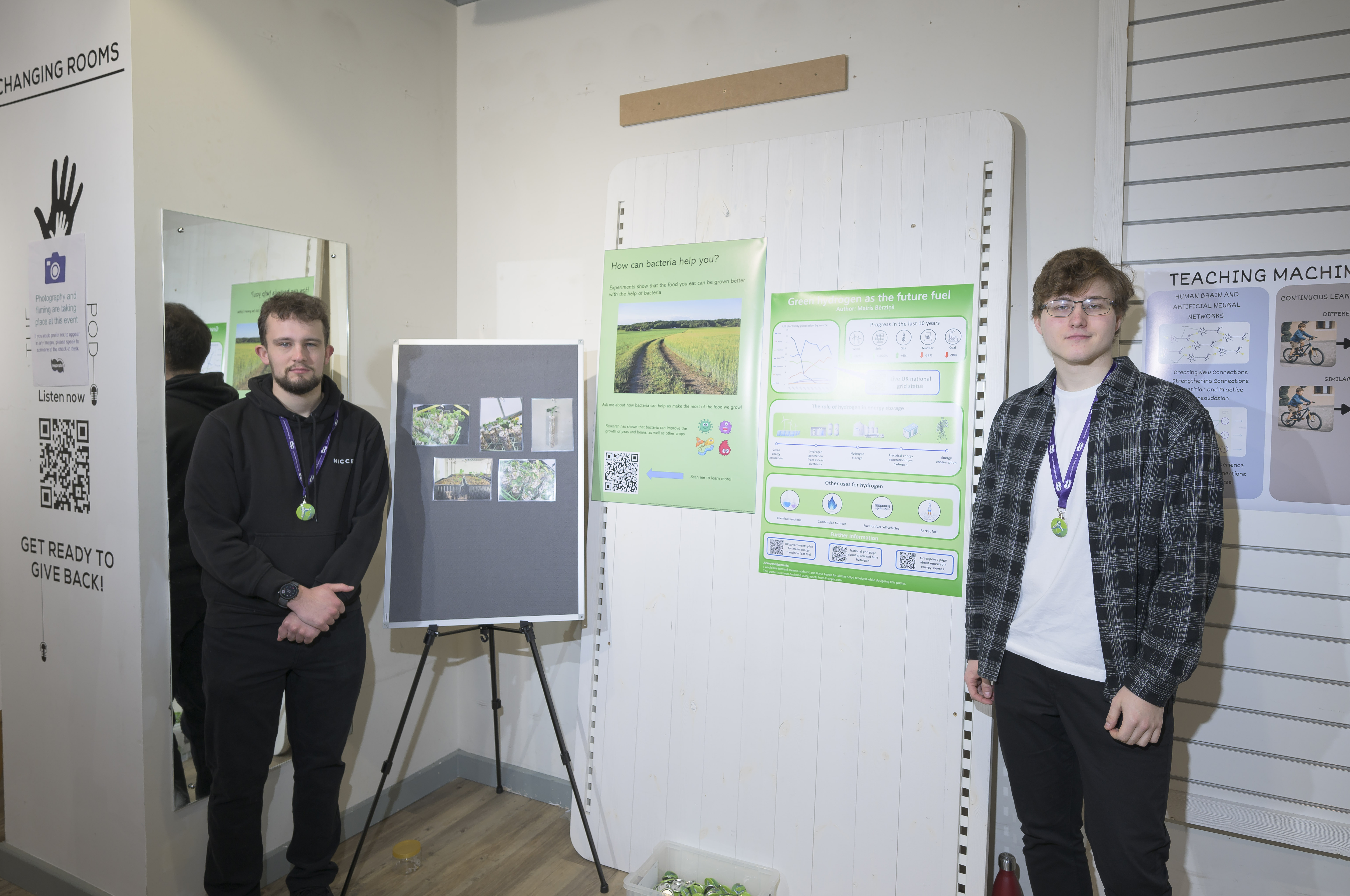 Two students standing with their posters and a pinboard with photos on it. 