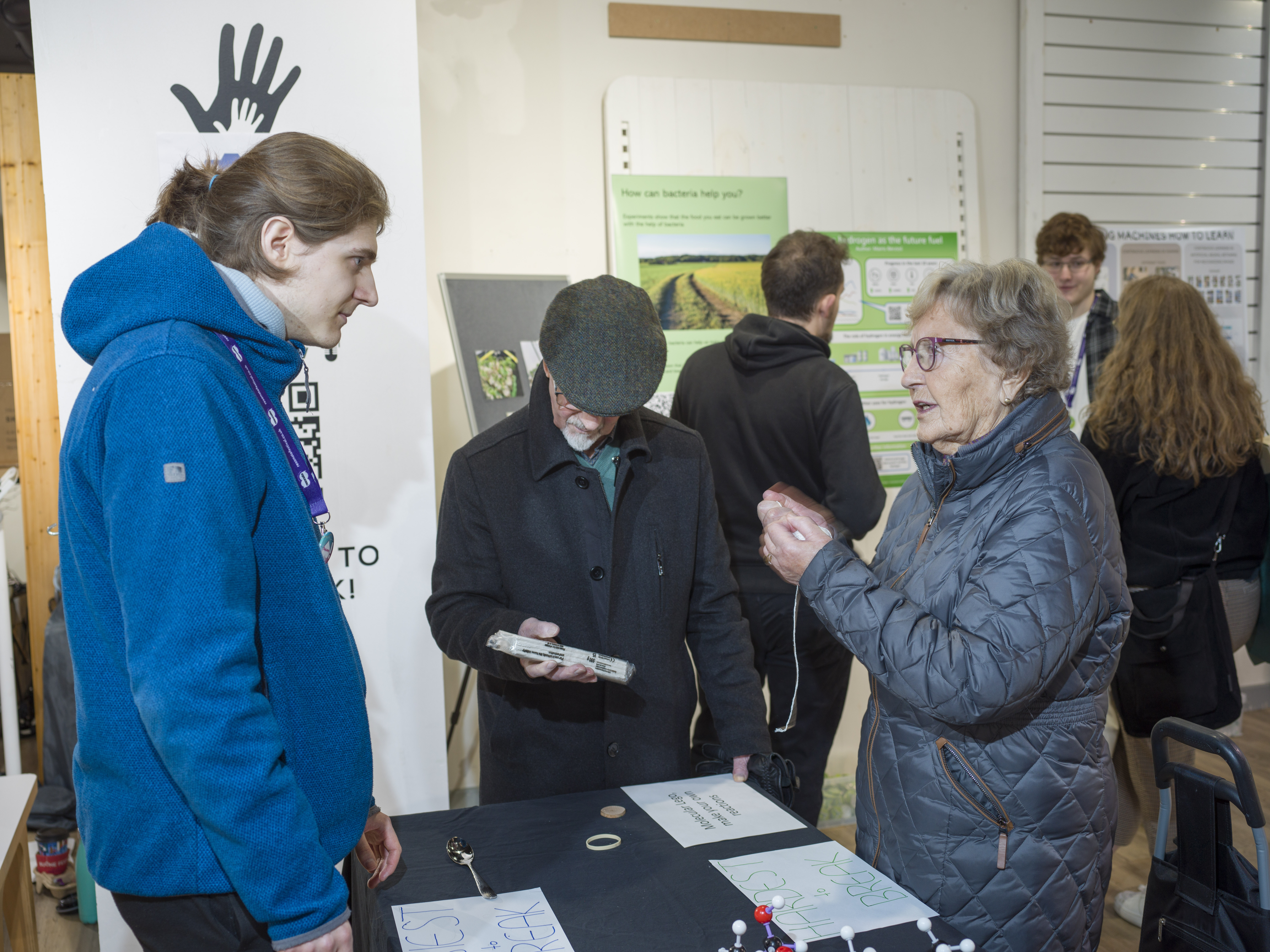 A student talks to two members of the public who are holding different objects to test their hardness.