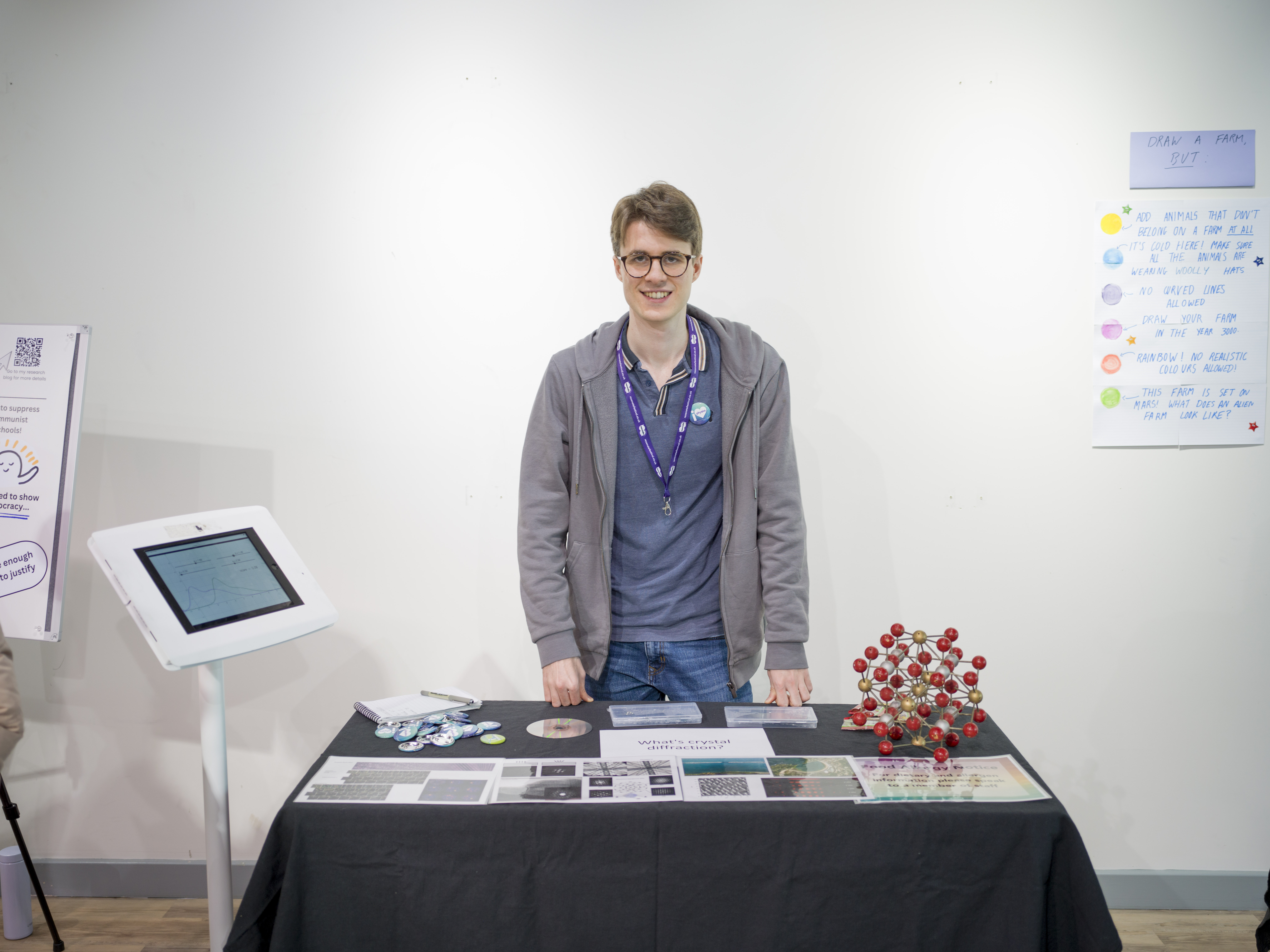 A student stands behind a table with a molecular model on it, lots of pictures and an iPad.