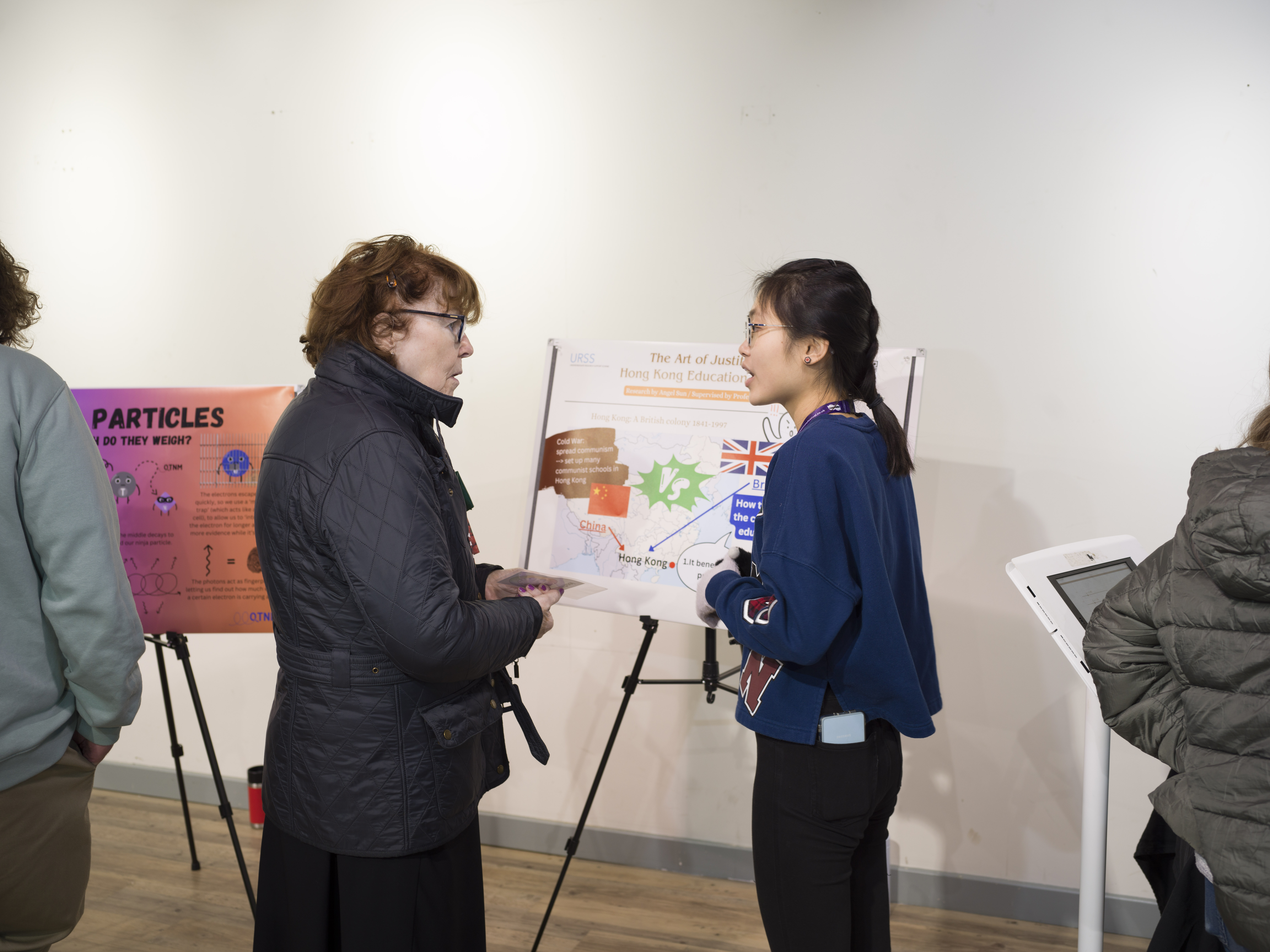A student talking to a member of the public in front of a landscape poster. 