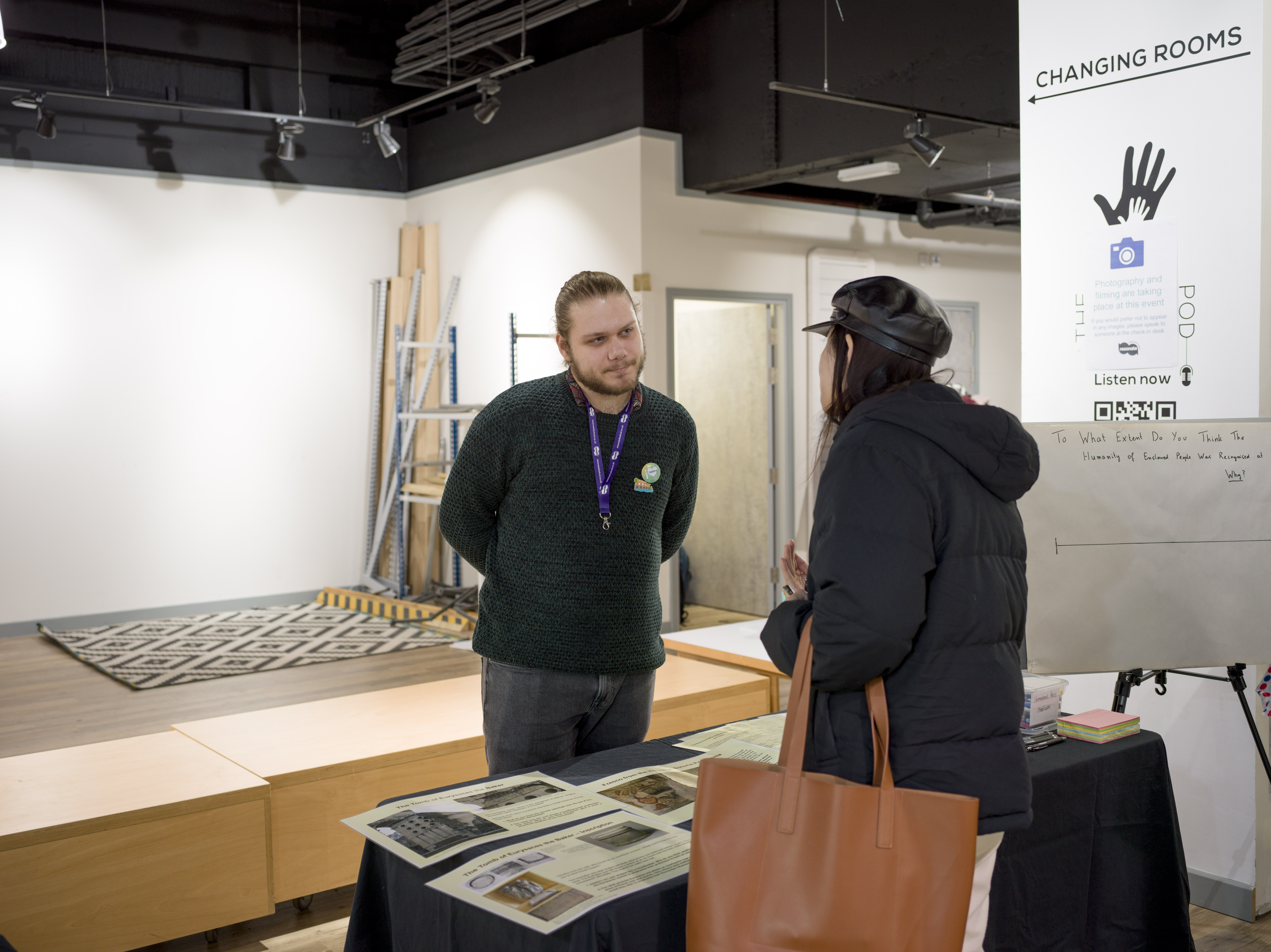 A student talks to a visitor over a table that displays pictures of ancient sources and monuments.