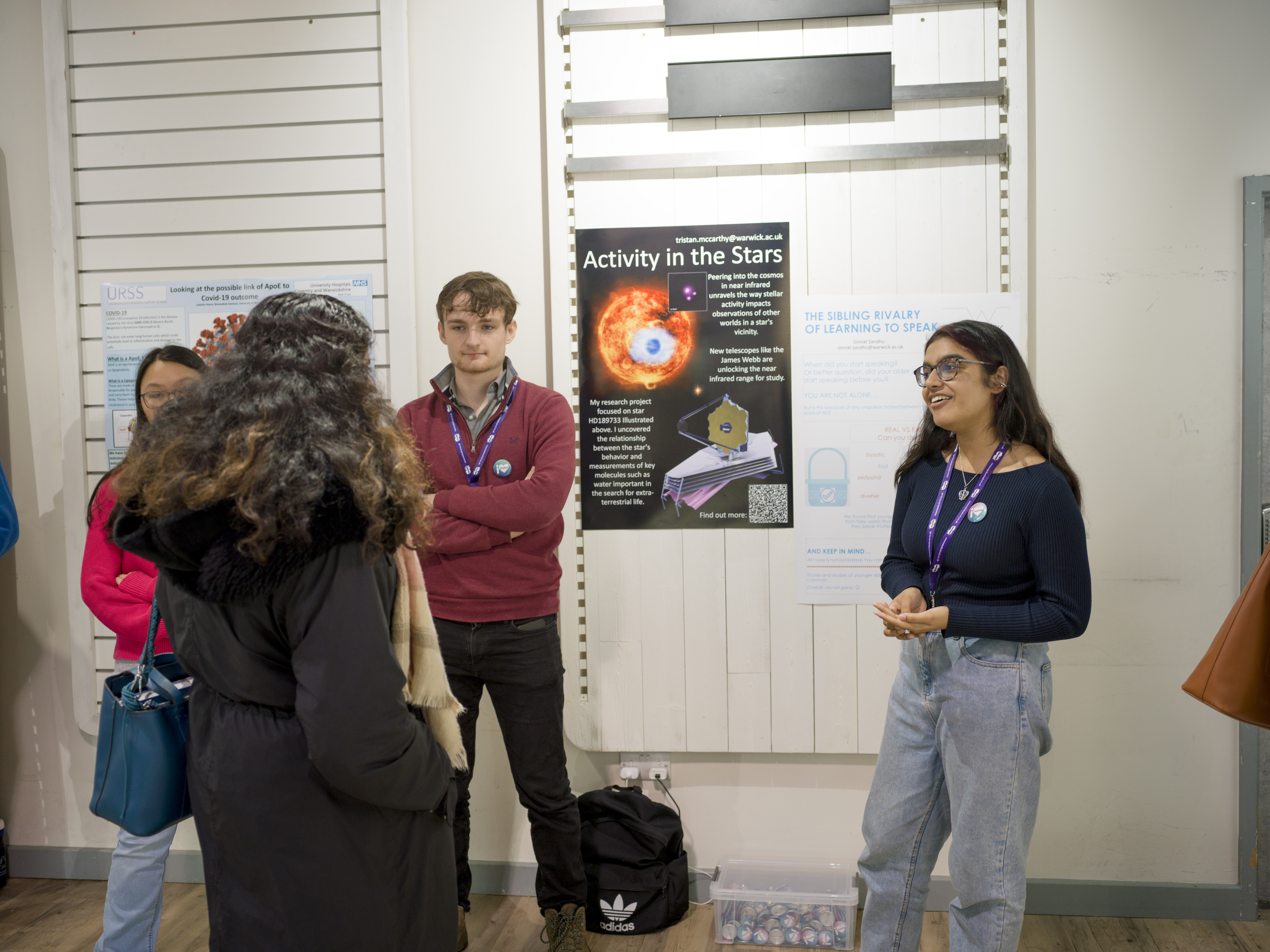 Two students talk to a visitor in front of their posters. 