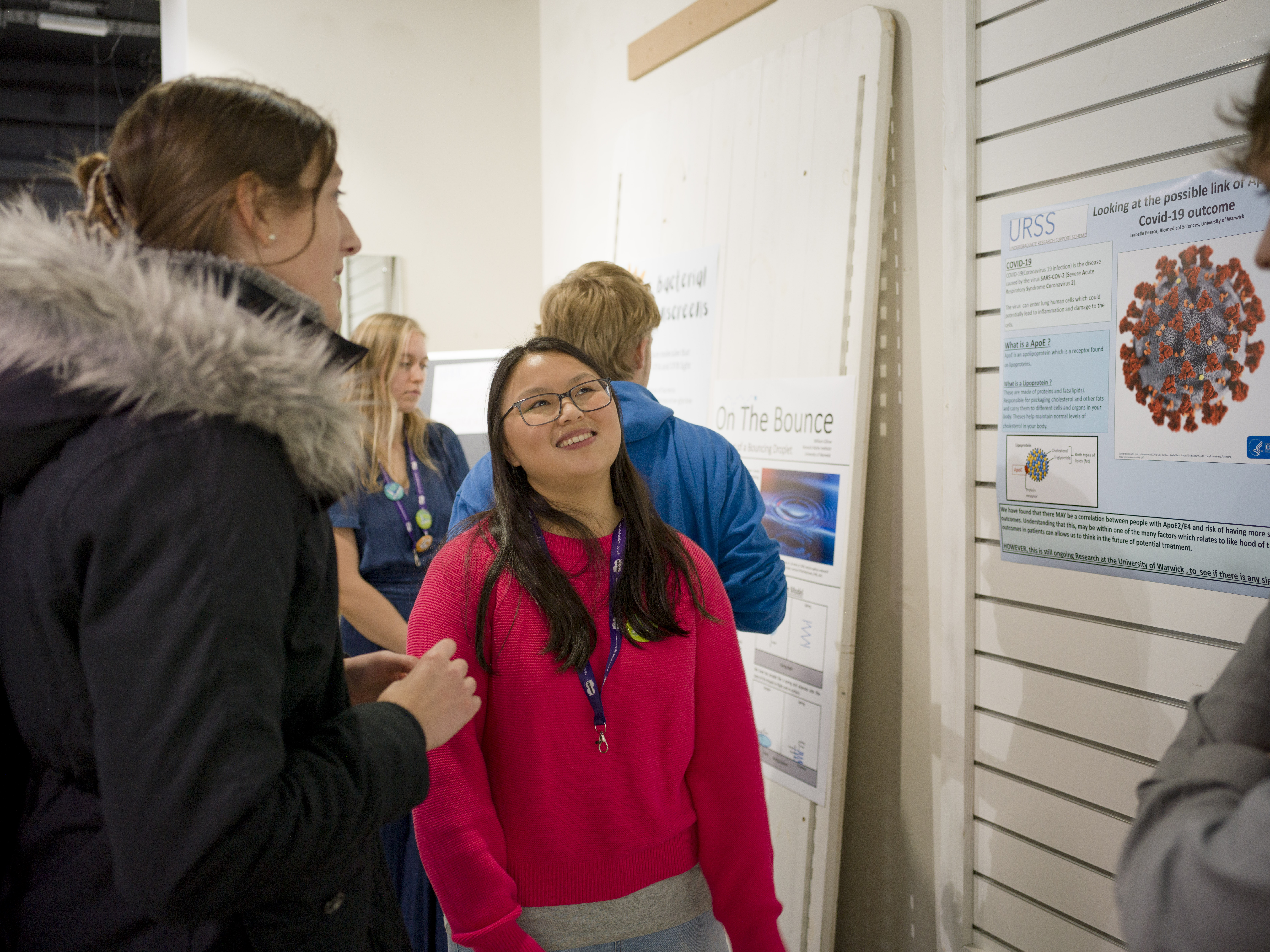 A student smiles next to their poster while talking to visitors. 