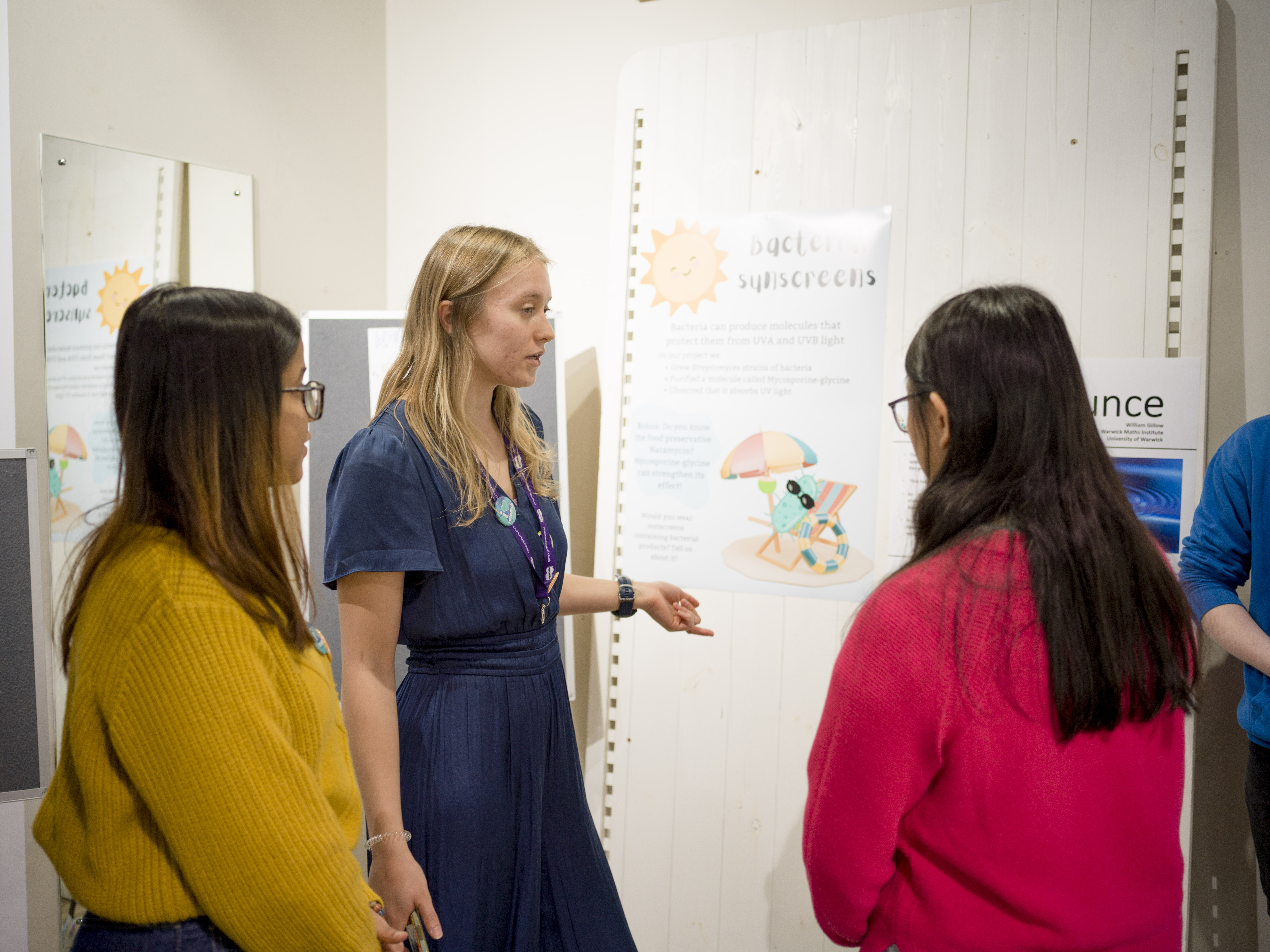 Three students talking together next to a poster. 