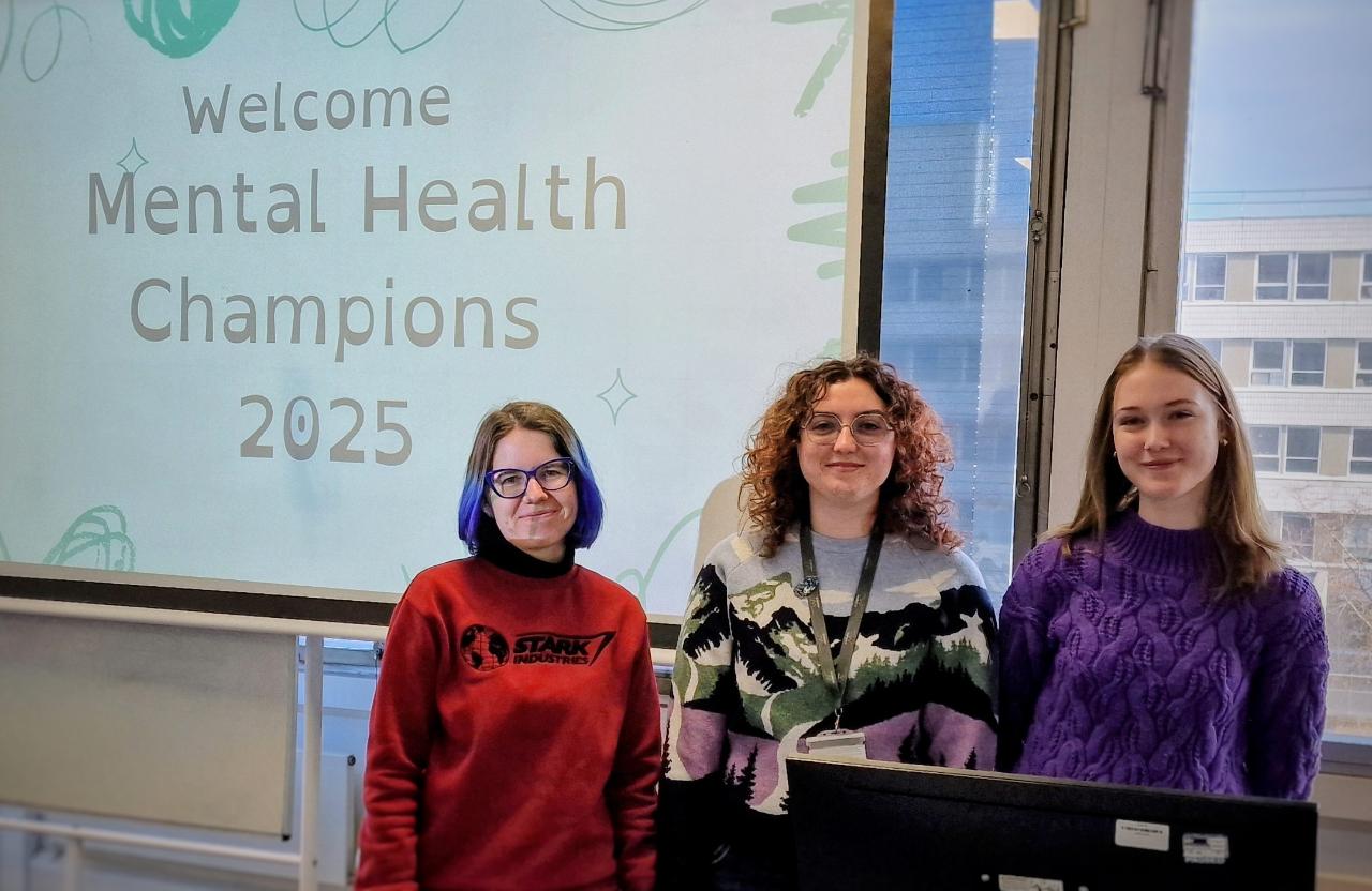 Ana, Ida and Caitlin in front of a screen that says 'welcome mental health champions 2025'